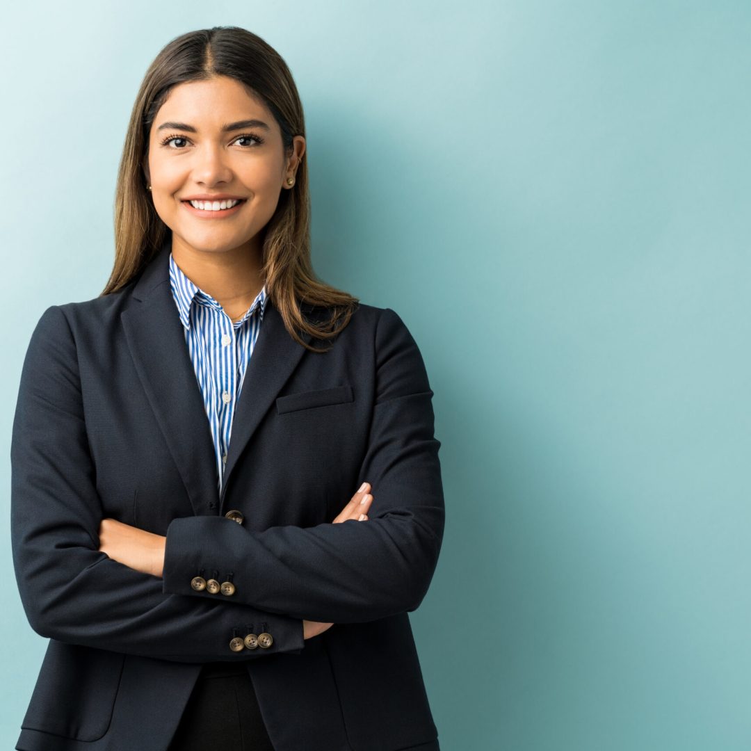 Happy Latin businesswoman standing with arms crossed against isolated background