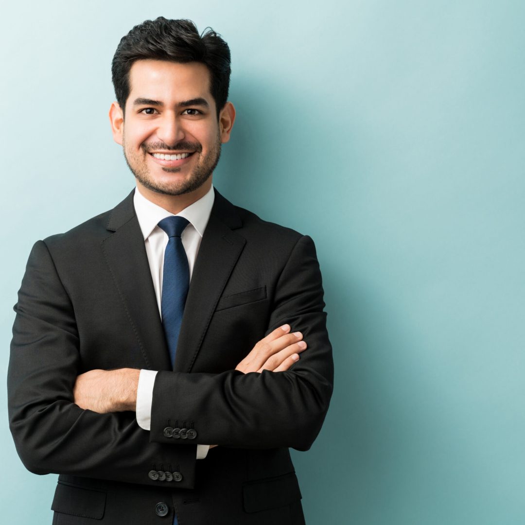 Smiling young male professional standing with arms crossed while making eye contact against isolated background